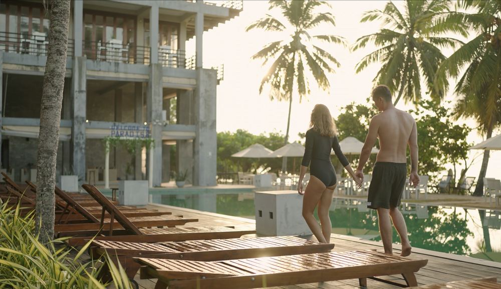 A couple walking past the pool at a resort in the evening light